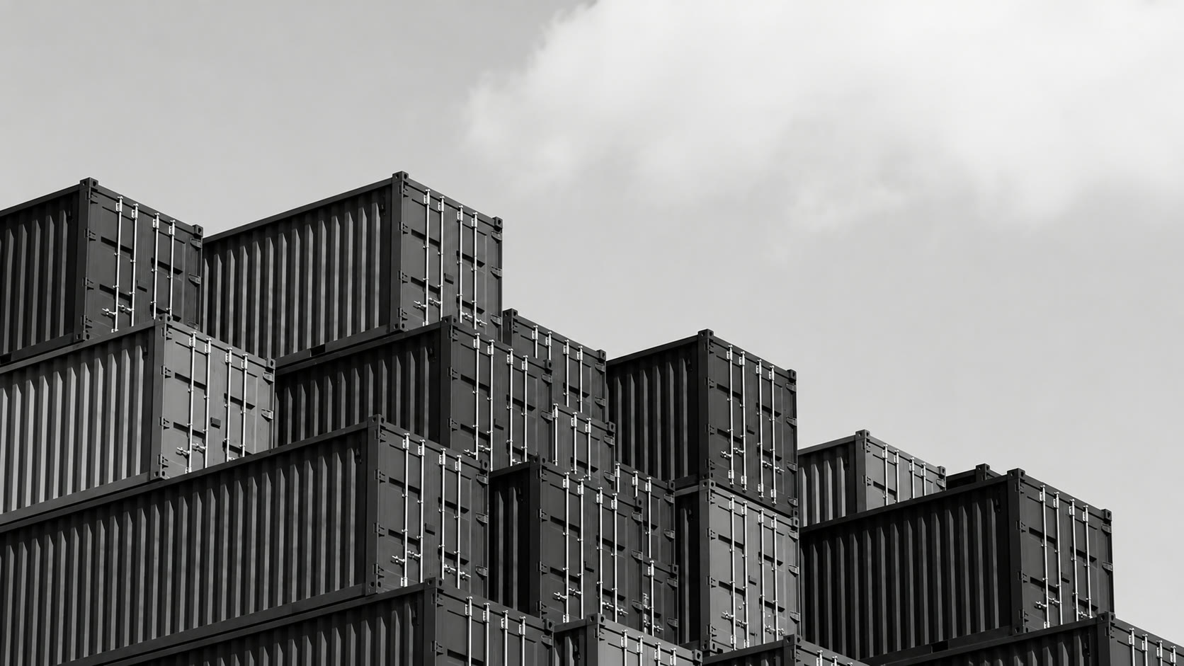 Stacked shipping containers against an open sky, in black and white