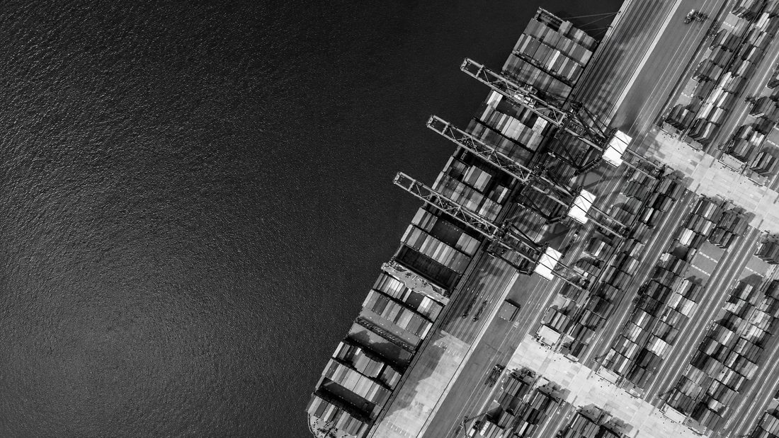 Aerial view of a container ship being worked by quay cranes alongside a stacked container terminal