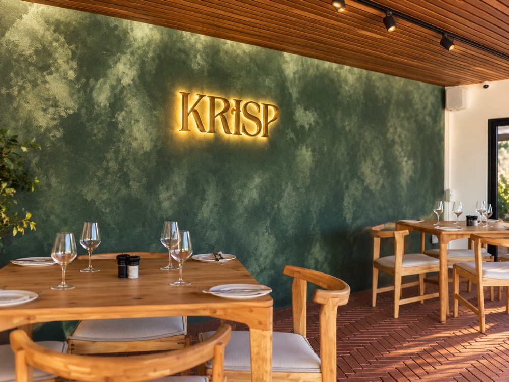 Interior of the KRiSP restaurant, backlit lettering on a deep green plaster wall above timber tables